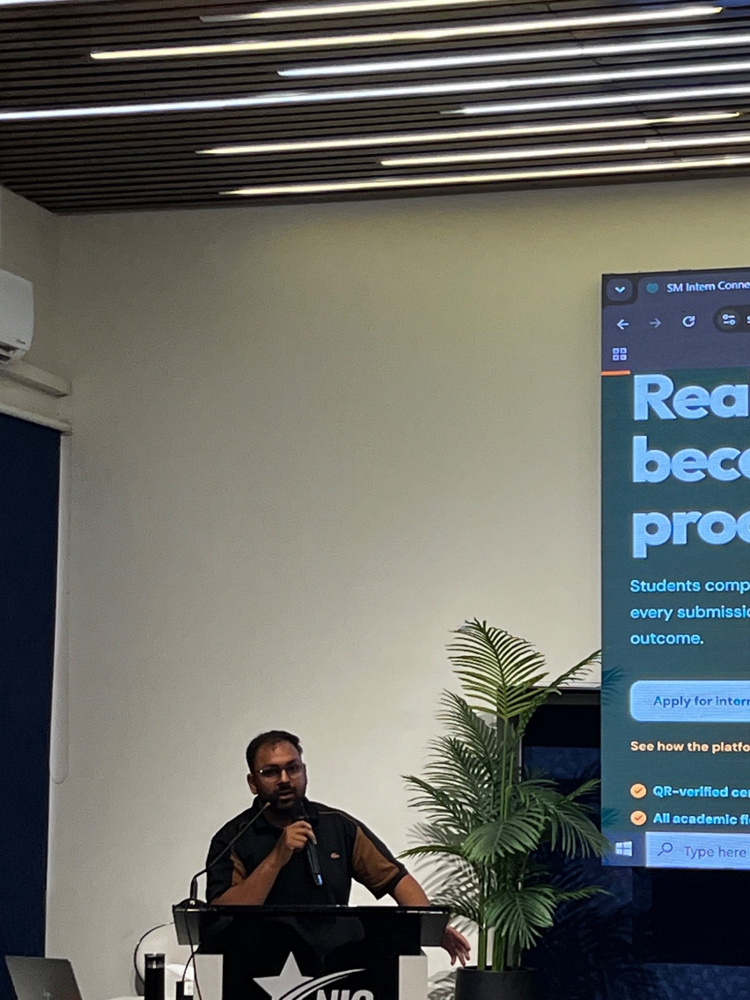 A speaker addressing attendees beside the SM Intern Connect presentation screen